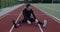 Male disabled sportsman with prosthetic running blades stretching back while sitting at sports field. With amputed leg