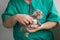 Male doctor with beard in green costume holds in hands and examins with stethoscope grey toy cat on the empty white background.