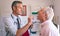 Male doctor checking senior male patient mouth with otoscope