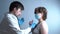 Male doctor checks the breath of a female patient in a medical mask on a gray background.