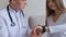 Male doctor explains to patient how to use smart Watch to monitor health and sit on couch in hospital`s office.