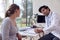 Male Doctor Or GP Wearing White Coat Examining Teenage Girl Listening To Chest With Stethoscope