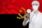 Male doctor with a stethoscope on the background of the silk national flag of Angola, the concept of national medical care, health