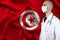 Male doctor with a stethoscope on the background of the silk national flag of Tunisia, concept of national medical care, health,