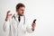 Male doctor with stethoscope in medical uniform holding smartphone, texting, looking nervously