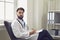 Male doctor in uniform sitting in armchair at his office. Medical specialist in clinic. Young general practitioner at