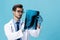 Male doctor in a white coat surgeon looks at an x-ray of a patient smile on a blue isolated background, copy space