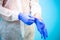 Male doctor in a white virus protective suit puts blue rubber gloves on his hands