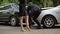 Male driver observing car damage, woman nervously walking, road accident