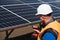 Male electrical engineer in a hard hat with electric wrench maintains solar panels at power plant.