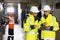 Male Electrical Engineers in Hard Hats Discuss New Project while Using Tablet Computer. They're Making Calculated