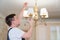 A male electrician changes the light bulbs in the ceiling light.