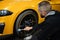 Male employee worker cleaning the wheel tire of modern yellow sport car by scrubbing brush