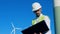 Male energetics worker is standing with his laptop near a wind turbine. Clean, eco friendly energy concept.