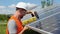 Male engineer in protective helmet installing solar photovoltaic panel system using screwdriver. Electrician mounting