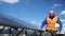 Male engineer stands on the stairs, takes off his hard hat and checks the solar panels with his hand for defects.