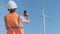 A male engineer takes a photo on a smartphone in a field on the background of a wind turbine. Inspects the wind turbine