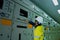 Male engineer wearing a yellow uniform and wearing a white safety hat, inspecting electrical systems in a large power plant