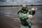 A male environmentalist in a green protective suit and gas mask takes a sample of water in a polluted lake. Waste from