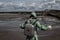 A male environmentalist in a green protective suit and gas mask takes a sample of water in a polluted lake. Waste from