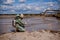 A male environmentalist in a green protective suit and gas mask takes a sample of water. The scientist is doing a