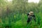 Male explorer makes observations in the wild with a spotting scope standing among the tall grass