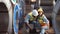 A male factory worker assists a female industrial worker who has an injured leg.