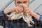 A male farmer caucasian handsome rural funny man in a shirt and overalls holds a two white brama chicken in his hands, close up