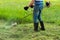 A male farmer mows the tall green grass in the spring with a trimmer. In summer, the gardener mows the lawn in the garden with a h