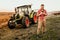 Male Farmer working on field using smartphone in modern agriculture - tractor and trailer background