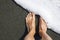 Male feet on the black volcanic sand covers with white sea foam. Minimalism. Geometric. Diagonal