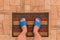 Male feet in blue house slippers stand on a foot mat on a brown tiled floor texture background, top view