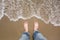 Male feet in jeans on sandy beach. Summer holiday. Beach, feet on sea sand with bubble float wave