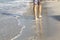 Male feet on the shore of a sandy beach on a sunny day. A young man walks along the edge of the water leaving footprints. Space