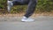 Male feet of sporty man running along road near forest at early autumn. Legs of young athlete sprinting fast along trail