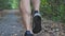 Male feet of young athlete running along trail in early autumn forest. Legs of sporty man jogging along path at nature