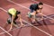 Male and female athlete in starting position at starting block o