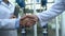 Male and female engineers in white coats shaking hands at factory, cooperation