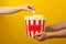 Male and female hands and bucket popcorn on yellow background