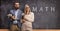 Male and female math teacher in front of a blackboard with text and formulas