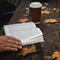 male female reads a book in autumn park drinks takeaway coffee coffee. Close-up over shoulder, blurred. top view, save space. Seen