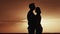 Male and female stand in an embrace in the morning near the sea. Silhouette of a loving family at sunrise or sunset