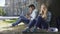 Male, female strangers sitting under tree, using cellphone, girl sighing heavily