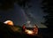 Male and female warming themselves around the fire at night camping above starry sky