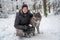 Male figure is pictured kneeling in a snowy landscape, accompanied by his canine