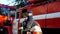 Male firefighter taking off helmet and balaclava against background of a fire engine. Portrait of young fireguard in