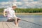 Male fisherman with a fishing rod sits on the pier