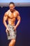 Male fitness model shows his physique in swimsuit om stage