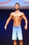 Male fitness model shows his physique in swimsuit om stage