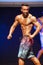 Male fitness model shows his physique in swimsuit om stage